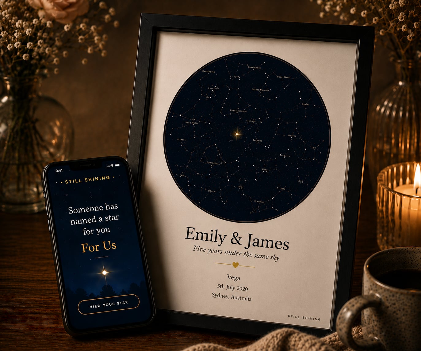 A framed Still Shining star map named for Emily and James, on a candlelit desk beside a phone showing the gift reveal
